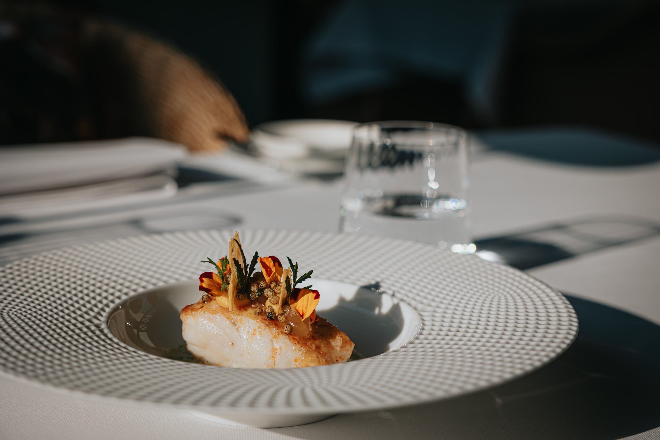 Fein angerichtetes Fischgericht mit essbaren Blüten im Restaurant Tante Anna auf edlem Porzellanteller.